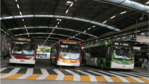Três ônibus em terminal de transporte.